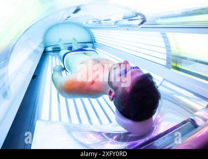 Jeune homme mince au solarium en instituts de beauté. Lit de bronzage intégral. Banque D'Images