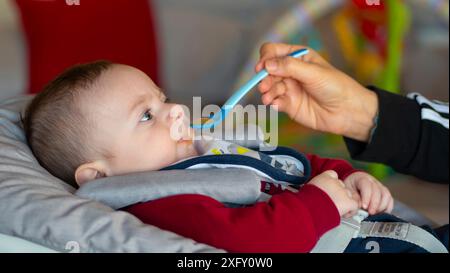 Gros plan d'un bébé de quelques mois commençant le sevrage en mangeant une purée de fruits. Banque D'Images