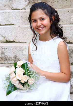 Souriante jeune fille en robe blanche pour la première Communion Banque D'Images