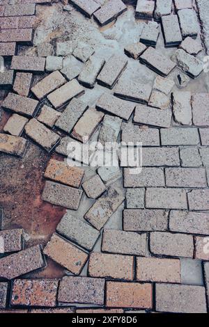 Chaussée mouillée après la pluie, verticale. Pavés cassés avec flaque d'eau. Finisseurs de briques humides. Trottoir de rue près. Vieux fond de dalles de pavage. Banque D'Images