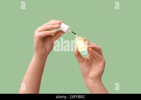 Mains féminines avec bouteille d'huile de cuticule sur fond vert Banque D'Images