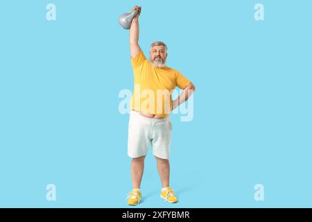 Homme mature heureux en surpoids avec kettlebell sur fond bleu. Concept de perte de poids Banque D'Images