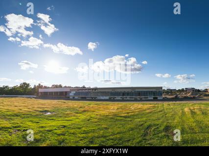 Un champ vert avec un vieux bâtiment par un chantier de construction et des machines Banque D'Images