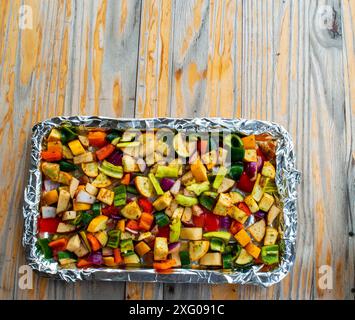 Un plan doublé de papier d'aluminium est rempli d'une variété de légumes colorés qui seront rôtis à la perfection. La casserole repose sur un vieux woo extérieur Banque D'Images