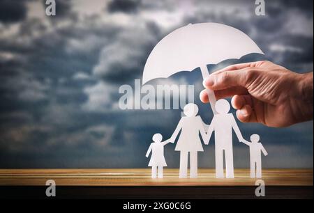 Concept de protection familiale avec la main couvrant une découpe d'une famille avec un parapluie sur une base en bois et des nuages avec de la pluie en arrière-plan. Banque D'Images