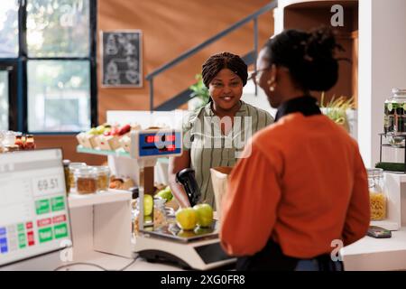 Dame noire souriante recevant l'aide d'un vendeur afro-américain à la caisse avec ses produits cultivés localement. Client à la caisse dans un magasin zéro gaspillage achetant des produits biologiques. Banque D'Images