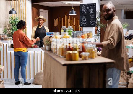 Le propriétaire d'entreprise afro-américain aide les clients au marché respectueux de l'environnement. Fruits frais, légumes et produits biologiques en vrac. Un service client efficace avec un emballage durable. Banque D'Images