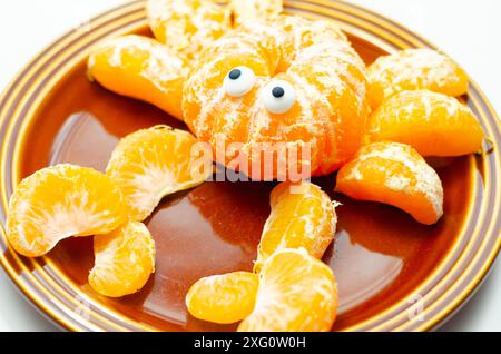 Une assiette de tranches d'orange avec un motif de crabe fait à partir des tranches. Le crabe a deux yeux et est assis sur une plaque brune Banque D'Images