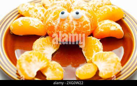 Une assiette de tranches d'orange avec un motif de crabe fait à partir des tranches. Le crabe a deux yeux et est assis sur une plaque brune Banque D'Images