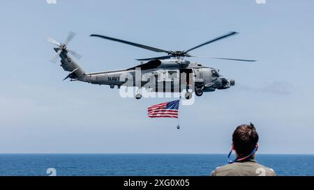 Un MH-60R Seahawk, affecté au Helicopter maritime Strike Squadron (HSM) 46, bat pavillon américain au-dessus du pont d'envol du porte-avions de classe Nimitz USS George Washington (CVN 73) alors qu'il était en route dans l'océan Pacifique, le 4 juillet 2024. George Washington est déployé dans le cadre de Southern Seas 2024, qui vise à améliorer la capacité, à améliorer l'interopérabilité et à renforcer les partenariats maritimes avec les pays de la zone de responsabilité du commandement sud des États-Unis par le biais d'échanges et de coopération conjoints, multinationaux et interagences. (Photo de l'US Navy par le spécialiste de la communication de masse 3rd Clas Banque D'Images