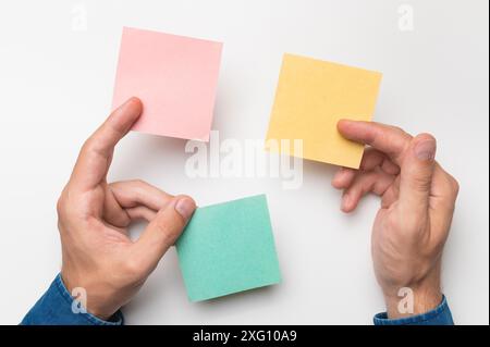 Mains des hommes tenant des autocollants vierges dans leurs doigts, blancs de différentes couleurs pour écrire des messages. Employé de bureau Banque D'Images