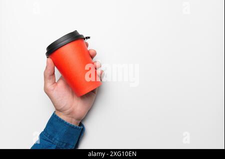 La main d'un homme dans une chemise tient une tasse de café rouge en papier sur un fond blanc Banque D'Images