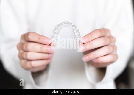 Gros plan de la main d'une femme tenant des aligneurs invisibles pour blanchir et redresser les dents sur un fond flou. Traitement orthodontique après Banque D'Images
