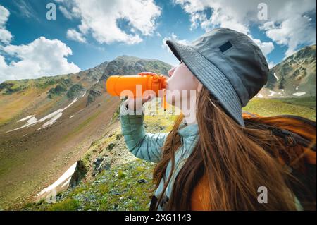 Randonneur féminin en bonne santé boit de l'eau lors d'une randonnée dans la nature. Belle jeune femme heureuse sur une randonnée avec une bouteille d'eau prenant une pause Banque D'Images