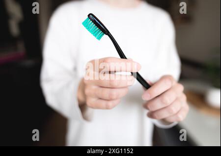 La main d'une femme avec une brosse à dents noire et verte sur un fond blanc tire une brosse vide propre dans le cadre, une fille sans visage Banque D'Images