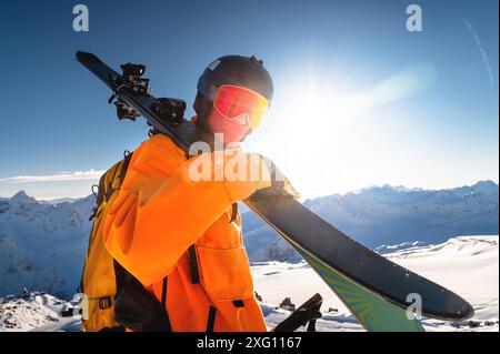 Heureux skieur tenant une paire de skis et regardant la caméra. Un gars avec des skis sur l'épaule se tient dans les montagnes couvertes de neige. Homme avec Banque D'Images