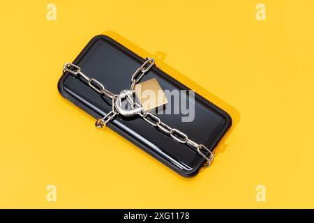 Concept de sécurité du téléphone. Smartphone verrouillé avec chaîne et cadenas sur fond jaune. Sécurité mobile et confidentialité des données Banque D'Images