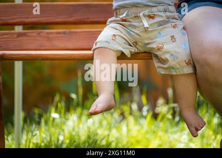 Concept de bébé grandir : gros plan des pieds de bébé pieds nus assis sur le banc du parc, heure d'été Banque D'Images