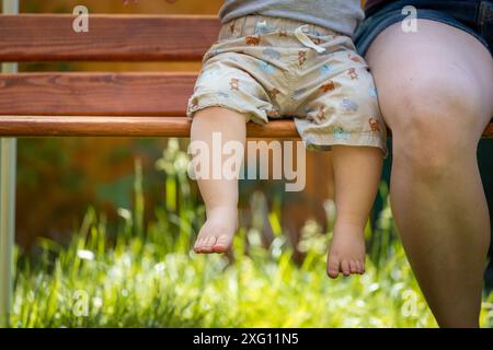 Concept de bébé grandir : gros plan des pieds de bébé pieds nus assis sur le banc du parc, heure d'été Banque D'Images