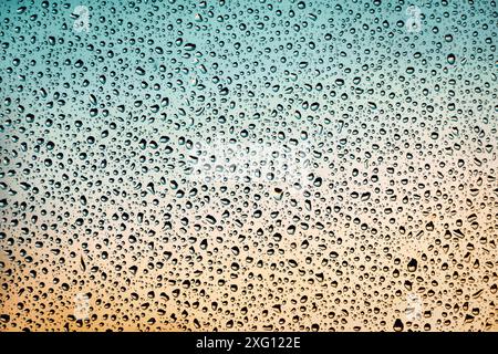 Fenêtre humide fond orange sarcelle, gouttes d'eau sur le verre, temps pluvieux, espace de copie Banque D'Images