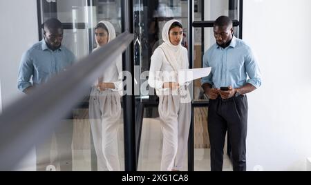 Collègues marchant au bureau, examinant des documents et utilisant un smartphone Banque D'Images