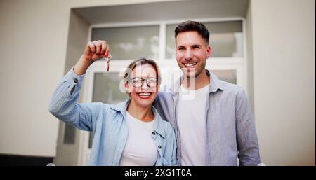 Heureux couple souriant avec les clés de maison en main - agents immobiliers guidant la jeune famille à l'achat de nouvelle maison Banque D'Images