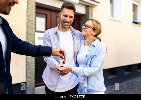 Agent immobilier remettant les clés à un jeune couple pour leur nouvelle maison. Transfert de propriété terminé. Banque D'Images