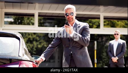 Gardes du corps professionnels ouvrant la porte de voiture de luxe pour homme d'affaires mature en dehors de l'événement d'entreprise - services de protection VIP en action. Banque D'Images