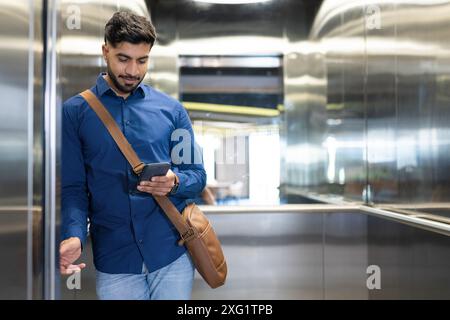 En utilisant le smartphone, homme avec le sac de messager debout dans l'ascenseur, vérifier les messages, copier l'espace Banque D'Images