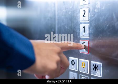 En appuyant sur le bouton de l'ascenseur, une personne en tenue d'affaires utilise l'ascenseur du bureau Banque D'Images