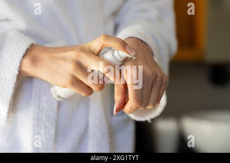 Application de lotion, femme en peignoir hydratant les mains à la maison Banque D'Images