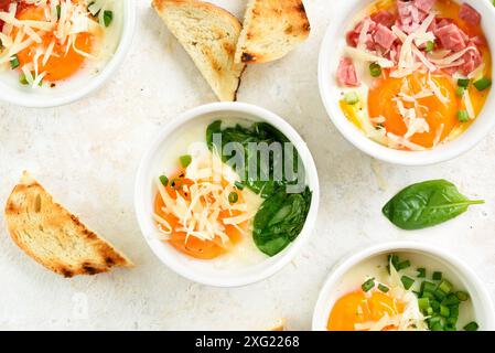 Vue rapprochée des oeufs en cocotte (oeufs cuits au four) dans des ramequins servis avec des toasts à tremper sur fond clair. Plat pour petit déjeuner ou déjeuner sain. T Banque D'Images