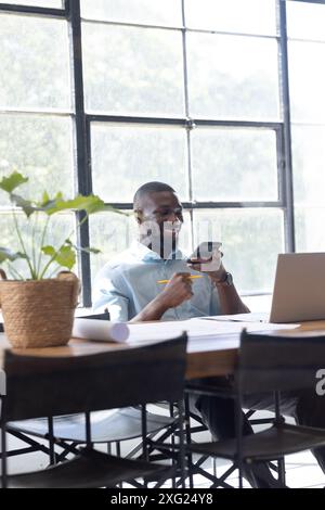 Homme d'affaires souriant utilisant smartphone et ordinateur portable tout en travaillant au bureau, copiez l'espace Banque D'Images