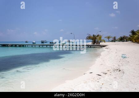 Une plage sur Fulidhoo avec des bateaux amarrés et une immense école de poissons (sombre) Banque D'Images