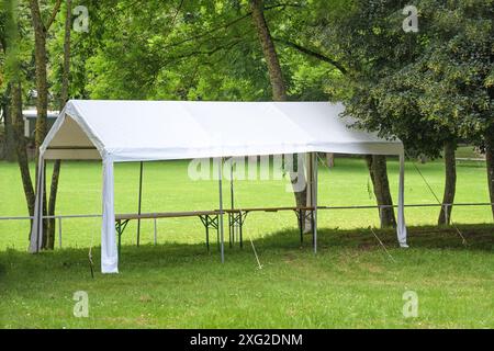 Tente de fête blanche vide installée sous les arbres sur une prairie dans un parc, préparation pour un événement de festival d'été, espace de copie, focus sélectionné Banque D'Images