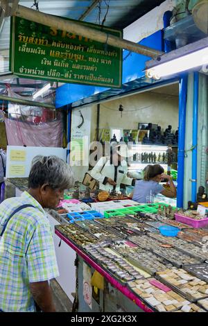 BANGKOK, THAÏLANDE - Stall de marché intérieur vendant des ornements bouddhistes avec un homme local regardant les articles à vendre. Banque D'Images