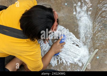 Une fille lave la tête d'une serpillière sur du béton Banque D'Images