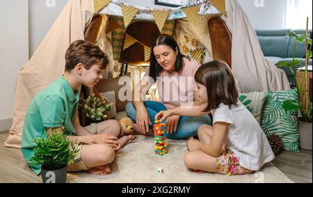 Heureuse mère et fils s'amusant tout en jouant avec le jeu de pièces empilables en bois devant la tente maison sur le salon. Famille monoparentale Banque D'Images