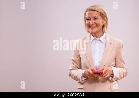 Portrait de femme d'affaires mature réussie utilisant le téléphone sur fond gris. Banque D'Images