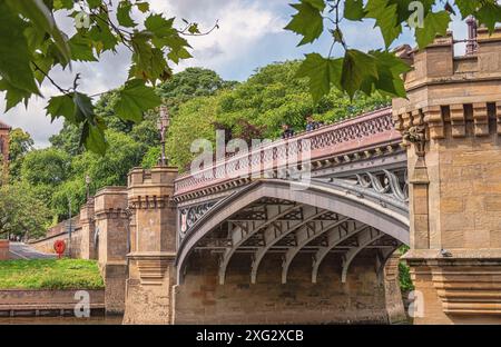 Un pont en pierre historique, orné de ferronnerie et de tours, s'étend sur une rivière. Les arbres sont en arrière-plan et un ciel nuageux est au-dessus. Banque D'Images