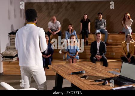 Vue arrière sur jeune enseignant afro-américain donnant un discours aux étudiants adultes l'écoutant attentivement, regardant heureux, Groupe de personnes dans le Backgro Banque D'Images