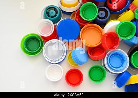 Les bouchons multicolores de bouteilles en plastique reposent sur une table en bois blanc dans un ordre chaotique Banque D'Images