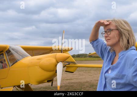 Femme blonde en lunettes sur le fond d'un aérodrome avec un avion jaune Banque D'Images