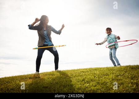 Cerceau, terrain et danse avec nounou et fille, jouets et amusement dans la nature pour l'activité de vacances. Garde d'enfants, liaison et herbe avec la personne féminine en automne Banque D'Images