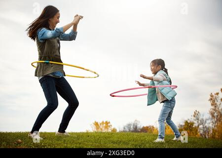 Maman, fille et danse avec cerceau dans la nature, jeu et terrain en automne pour l'activité. Enfant, ensemble et liaison avec une personne féminine ou mère avec une fille Banque D'Images