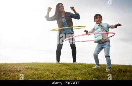 Cerceau, herbe et parc avec mère et fille, jouets et amusement dans la nature pour l'activité de vacances. Garde d'enfants, liaison et champ avec la personne féminine en automne Banque D'Images