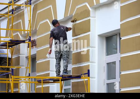 Le travailleur répare le mur du bâtiment debout sur la plate-forme de levage. Peinture de constructeur de la façade de la maison, travaux de construction et de réparation Banque D'Images