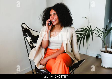 Femme latine africaine sur un appel téléphonique, souriant à la maison Banque D'Images