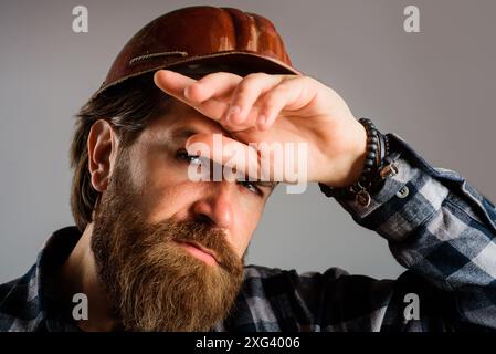 Gros plan portrait d'un ouvrier de construction fatigué en chemise à carreaux et casque de protection. Constructeur masculin fatigué dans le casque de protection essuie la sueur du front. Dur Banque D'Images