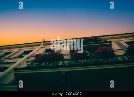 Un magnifique bâtiment européen, avec des fleurs rouges fleurissant sur les balcons, se dresse sur fond d'un ciel nocturne clair, alors que le soleil se couche. Journe Banque D'Images